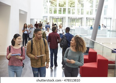 Students holding tablets and phone talk in university lobby