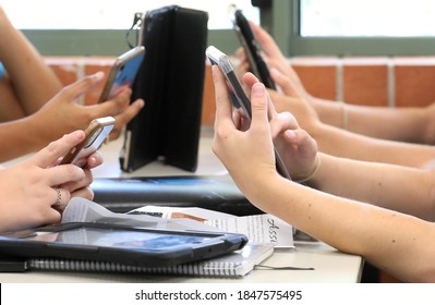 Students holding and using a range of digital devices. Mobile cell phones tablets and technology being handled by students at a desk in a school educational setting - Powered by Shutterstock