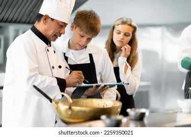 Students are learning to cook in a culinary institute with a standard kitchen and complete equipment. And have a professional chef as a trainer. - Shutterstock ID 2259350021
