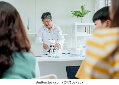 Students' learning in science classroom. Dedicated teacher holding test tubes with blue and green liquids demonstrates scientific experiment to attentive students in sunny classroom. - Powered by Shutterstock