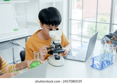 Students' learning in science classroom. Focused young students experiment with chemicals, using flasks and test tubes, with microscope and laptop on clean white desk in classroom. - Powered by Shutterstock