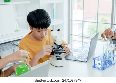 Students' learning in science classroom. Focused young boy students experiment with chemicals, using flasks and test tubes, with microscope and laptop on clean white desk in classroom. - Powered by Shutterstock