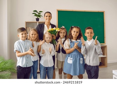 Students make a little surprise for their teacher. Group portrait of happy children and a woman with flowers standing in front of the blackboard in the classroom. Back to school, Teacher's Day concept - Powered by Shutterstock