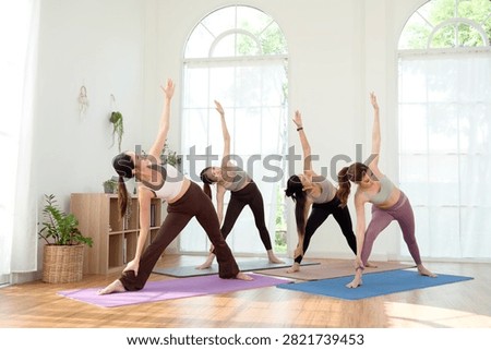 Students practice revolved triangle pose during a yoga class in a bright and open studio.