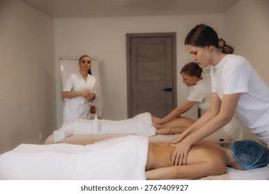 Students practicing back massage therapy on clients in a bright spa classroom setting with an instructor observing