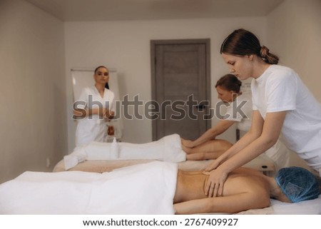 Students practicing back massage therapy on clients in a bright spa classroom setting with an instructor observing