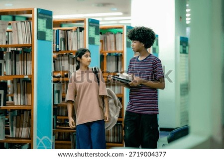 Students selecting reading materials inside library showing independent learning curiosity research habit education journey. Students talking while walking through aisel.