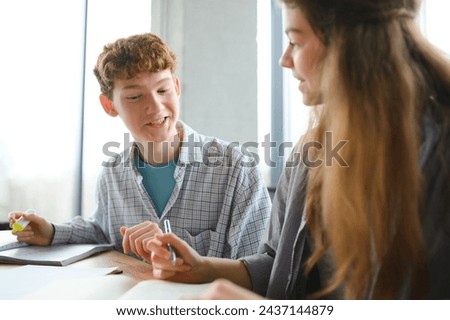 students sit at shared desk making notes studying together at university.
