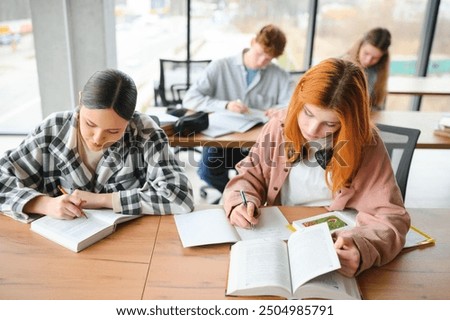students sit at shared desk making notes studying together at university.