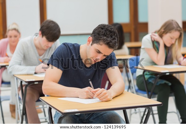 Students sitting in an exam hall doing an exam\
in university