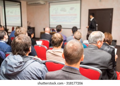 Students Sitting In A Lecture Room With Teacher In Front Of The Class With White Projector Slide Screen