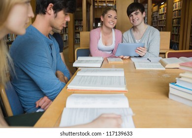 Students sitting at library table smiling while holding a tablet pc in college