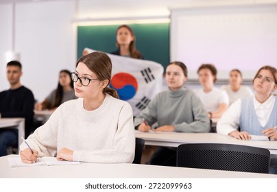 Students study in classroom, teacher stands behind with South Korean flag