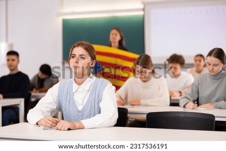 Students study in classroom, teacher stands behind with flag of Catalonia