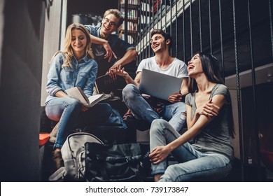 Students are studying in library. Young people are spending time together. Reading book, working with laptop and communicating while sitting on stairs in library. - Shutterstock ID 739173847