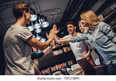 Students are studying in library. Young people are spending time together. Young handsome men and attractive women are working together. Giving five to each other