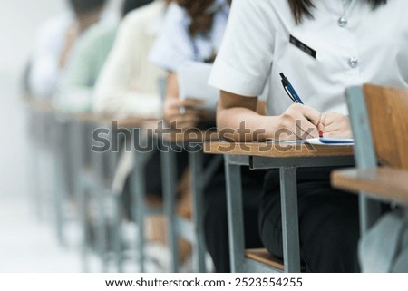Students Taking Exam in Classroom Setting. Students in uniforms are seated in a classroom, writing answers during an exam, highlighting focus and academic testing.