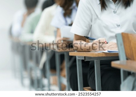 Students Taking Exam in Classroom Setting. Students in uniforms are seated in a classroom, writing answers during an exam, highlighting focus and academic testing.