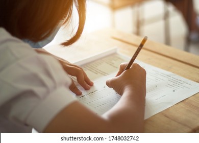 Students in uniform are doing the test in the classroom. Close up hand holding a pencil to write the answer to the exam on wooden table. Evaluation of learning for educational development