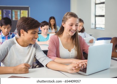 Students Using Digital Tablet And Laptop In Classroom At School