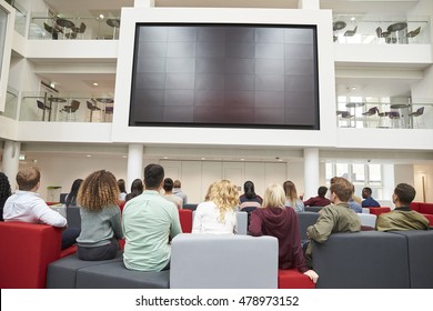 Students watching big screen in university atrium, back view