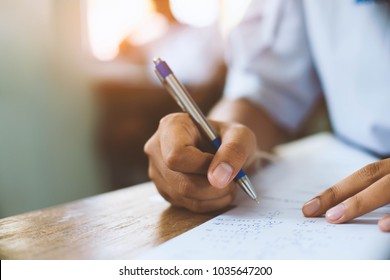 Students writing pen in hand doing exams answer sheets exercises in classroom  with stress.