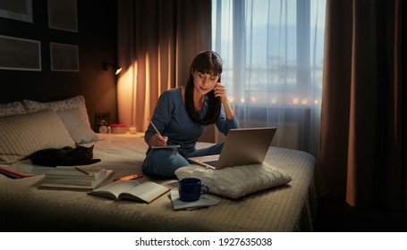 Studing At Home Online. Pretty Young Woman Using Laptop While Sitting On The Bed At Night Time.