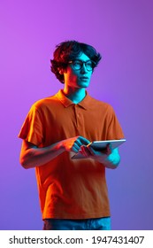 Studing  working  Young man in glasses using tablet isolated multicolored background in neon light  Concept human emotions  facial expression  youth culture  digital life  Copy space for ad 