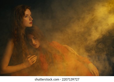 Studio Art Portrait Of Two Beautiful Redhead Freckled Women Posing In Smoke, Darkness And Warm Light. Copy, Empty Space For Text
