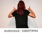 A studio back view close-up shot of an unrecognizable young Caucasian redhead woman showing the thumbs up with both hands