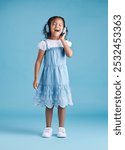 Studio, child and singer with headphones for dancing, hearing and music with sound for audio track. Happy person, girl and singing with technology for listening, song and blue background with mockup