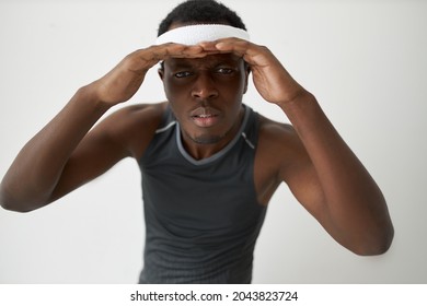 Studio Close-up Portrait Of African Man In Sportswear During Training, Holding Both Hands Over Head Peering Straight Into Camera With Unsatisfied Face, Trying To Look Closely And See More