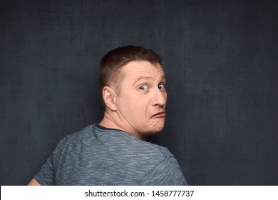 Studio Close-up Portrait Of Frightened Fair-haired Caucasian Man Taken By Surprise While Doing Something Secret, Turning Round And Looking With Discontent Out From Back At Camera, Over Gray Background