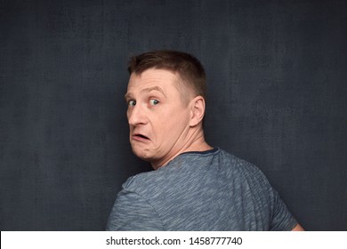 Studio Close-up Portrait Of Frightened Fair-haired Caucasian Man Caught Off Guard While Doing Something Secret, Turning Round And Looking With Discontent Out From Back At Camera, Over Gray Background