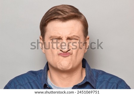 Studio close-up portrait of funny disgruntled blond mature man grimacing and making goofy crazy face, looking disgusted. Headshot over gray background