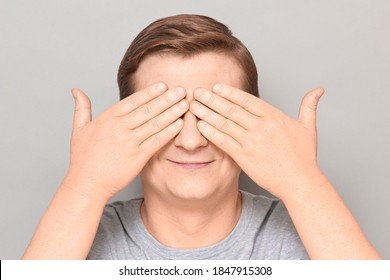 Studio Close-up Portrait Of Happy Optimistic Blond Mature Man Covering Eyes With Both Hands, Not Wanting To See Something Or Waiting Surprise, Smiling Cheerfully. Headshot Over Gray Background