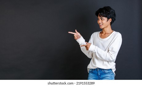 Studio Closeup Shot Of Asian Young LGBTQ Gay Glamour Bisexual Homosexual Male Model In Casual Outfit Standing Smiling Holding Two Hands And Fingers Pointing Blank Copy Space On Black Background.