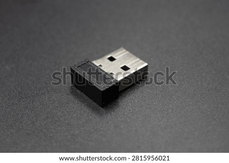 Studio close-up shot of a compact black nano USB receiver dongle for wireless mouse and keyboard isolated on a dark gray surface.