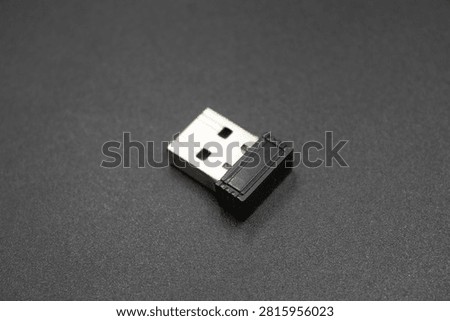 Studio close-up shot of a compact black nano USB receiver dongle for wireless mouse and keyboard isolated on a dark gray surface.