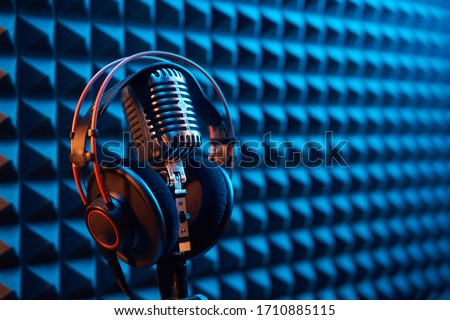 Studio condenser microphone with professional headphones on acoustic foam panel background with blue and orange light, copy space on right