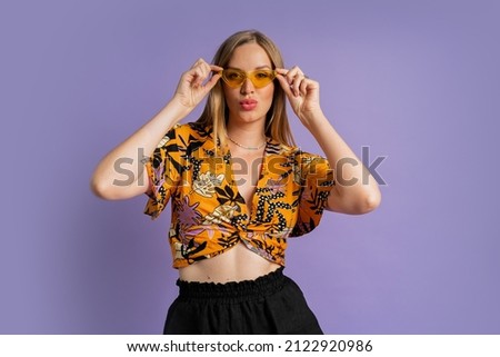 Studio fashion photo of pretty blond woman in stylish top and  linen shorts posing on purple background. 