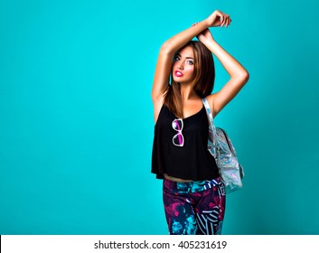 Studio fashion trendy portrait of sexy stunning fit woman, sportive smart casual outfit, colorful leggings, silver backpack, blue background. 