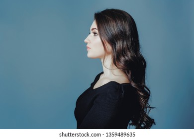 Studio gray background dark black clothes portrait girl evening reception profile side brunette hair looks edge frame. Blue cyan toned photo.