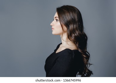 Studio gray background dark black clothes portrait girl evening reception profile side brunette hair looks edge frame.