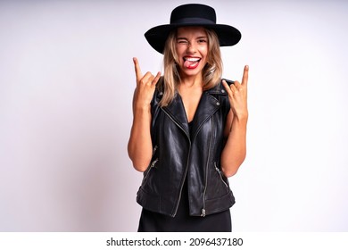 Studio grunge portrait of blonde sexy woman wearing black dress, hat and leather vest posing on white background. Free spirit, rock n roll style, having fun.