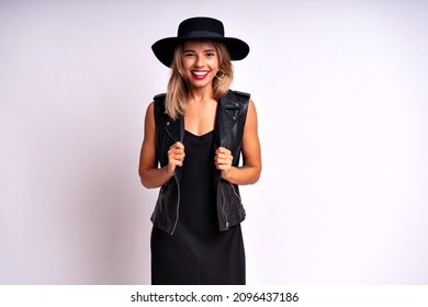 Studio Grunge Portrait Of Blonde Sexy Woman Wearing Black Dress, Hat And Leather Vest Posing On White Background. Free Spirit, Rock N Roll Style, Having Fun.