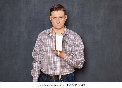 Studio half-length portrait of focused fair-haired young man wearing checkered shirt, holding big closed book in one hand over chest, looking with serious expression at camera, over gray background - Shutterstock ID 1515319349