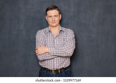 Studio half-length portrait of satisfied confident caucasian fair-haired man wearing shirt, holding arms crossed on chest, smiling slightly, looking calmly at camera, standing over gray background - Shutterstock ID 1529977169