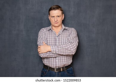 Studio half-length portrait of serious focused fair-haired caucasian man wearing checkered shirt, holding arms crossed on chest, looking strictly at camera, standing over gray background - Shutterstock ID 1522009853