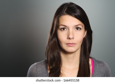 Studio Head And Shoulders Portrait On Grey Of A Beautiful Serious Young Woman Looking Directly At The Camera